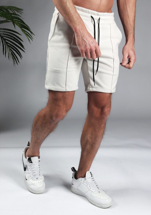 Rechter zijaanzicht comfortabele heren chino shorts in off white, met skinny fit en gemaakt van luxe stretch stof. Voorzien van twee broekzakken en rekbare taille met zwart trekkoord. Gecombineerd met witte sneakers.