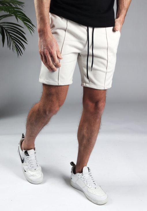 Vooraanzicht comfortabele heren chino shorts in off white, met skinny fit en gemaakt van luxe stretch stof. Voorzien van twee broekzakken en rekbare taille met zwart trekkoord. Gecombineerd met witte sneakers en een zwart T-shirt.