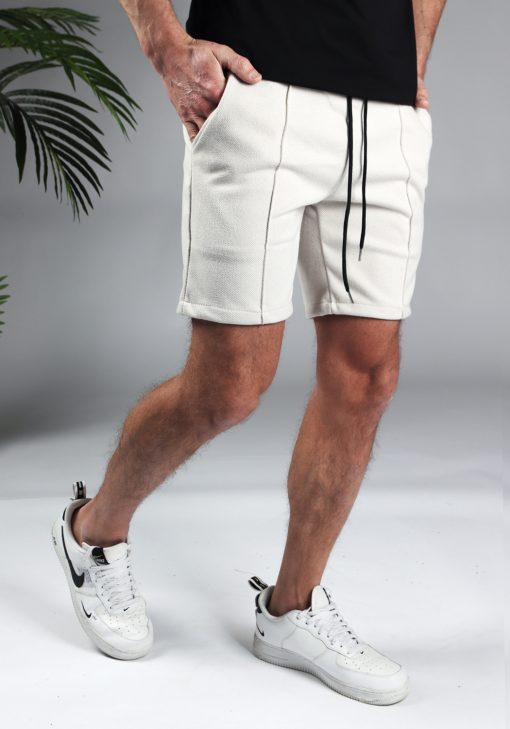 Rechter zijaanzicht comfortabele heren chino shorts in off white, met skinny fit en gemaakt van luxe stretch stof. Voorzien van twee broekzakken en rekbare taille met zwart trekkoord. Gecombineerd met witte sneakers en een zwart T-shirt.