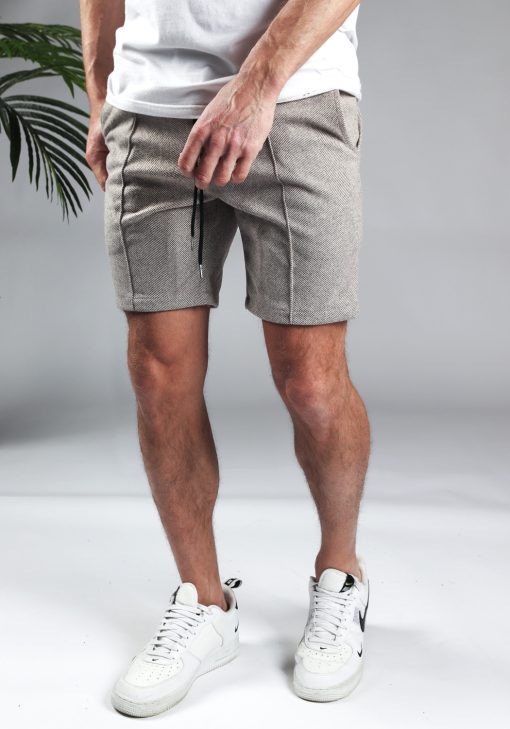 Linker zijaanzicht comfortabele heren chino shorts in zandkleur, met skinny fit en gemaakt van luxe stretch stof. Voorzien van twee broekzakken en rekbare taille met zwart trekkoord. Gecombineerd met witte sneakers en een wit T-shirt.