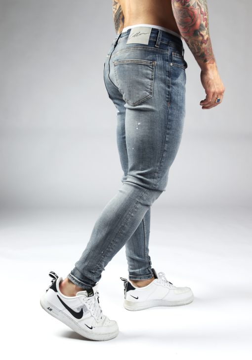 Achterkant licht blauwe denim heren skinny jeans met verfspetters. Voorzien van twee broekzakken, twee kontzakken, knoopsluiting en riemlussen.