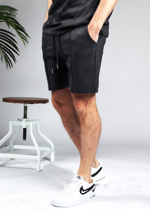 Zijaanzicht comfortabele heren chino shorts in zwarte kleur, met skinny fit en gemaakt van luxe stretch stof. Voorzien van twee broekzakken en rekbare taille met trekkoord. Gecombineerd met een zwart T-shirt en witte sneakers.