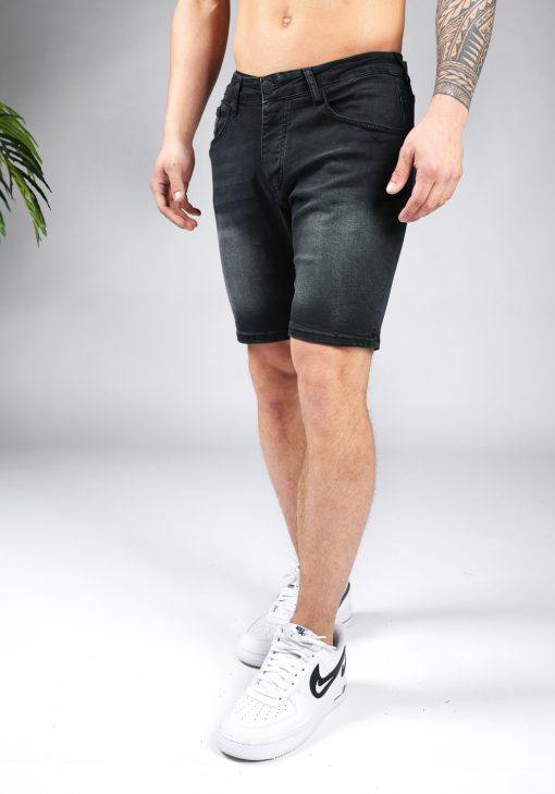 Schuin linker vooraanzicht van het onderlichaam van een model gekleed in zwarte jean shorts gecombineerd met witte sneakers.