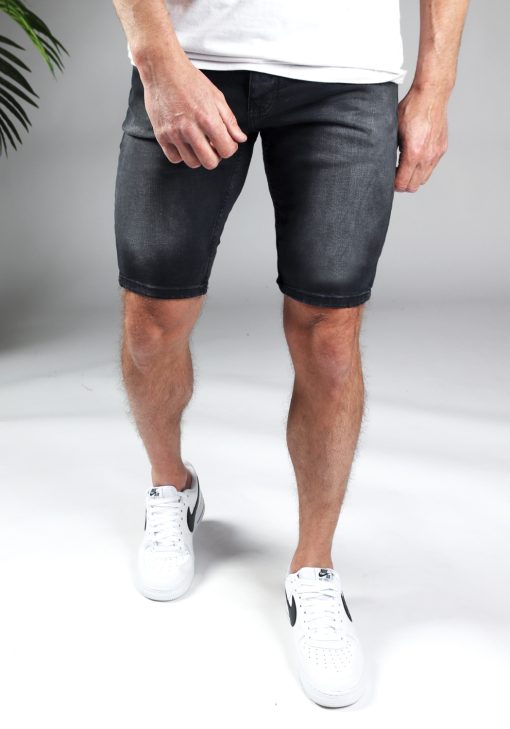 Vooraanzicht van het onderlichaam van een model gekleed in zwarte jean shorts gecombineerd met witte sneakers en een wit shirt. Het model heeft zijn armen losjes langs zich.