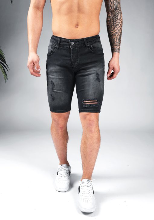 Vooraanzicht van model gekleed in zwarte jean shorts met damaged details in combinatie met witte sneakers.