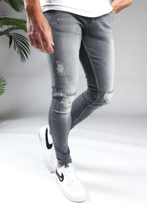 Rechter zijkant grijze damaged denim heren skinny jeans met scheuren en verfspetters.