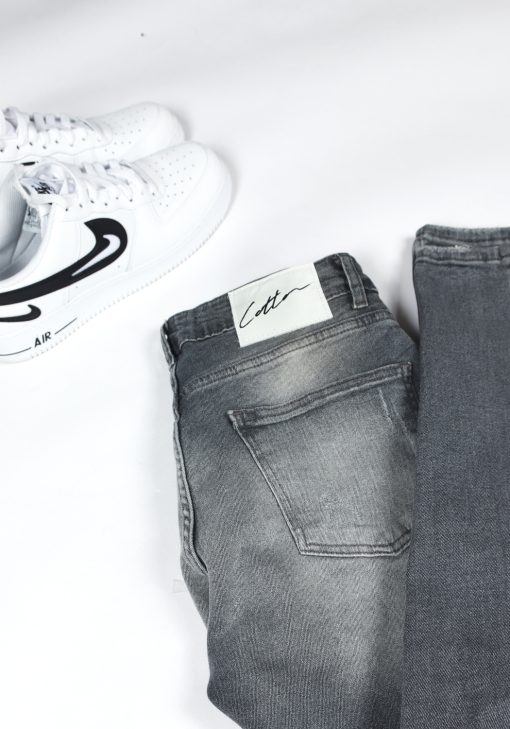 Close up logo op de achterkant van grijze damaged denim heren skinny jeans met scheuren en verfspetters.