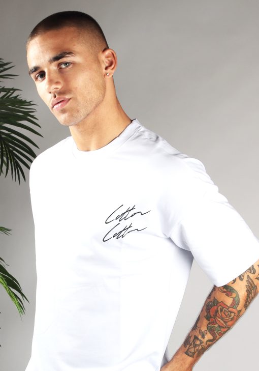 Close-up van heren T-shirt in witte kleur, met ronde hals en een oversized pasvorm. Het T-shirt is voorzien van twee Cotton-logo's in het zwart onder elkaar op de linkerborst.