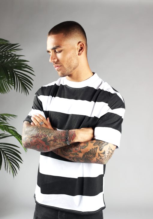 Vooraanzicht van model gekleed in zwart wit gestreepte t-shirt. De strepen zijn dik en lopen horizontaal. Het model heeft zijn handen voor zich over elkaar.