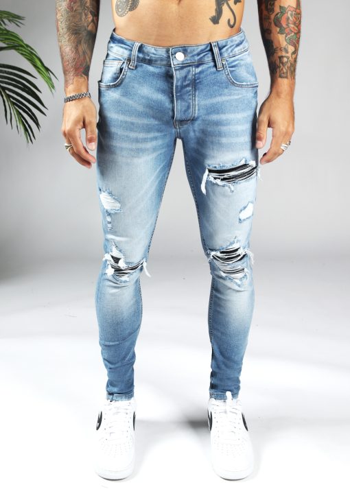 Voorkant lichte denim heren skinny jeans met met damaged afwerking, gemaakt van stretch stof. Voorzien van twee zakken aan de voorzijde, twee kontzakken, knoopsluiting en riemlussen.