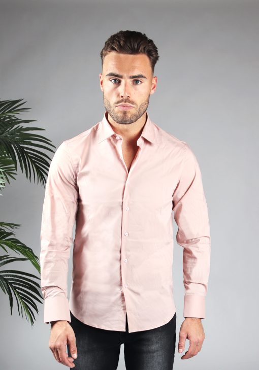 Vooraanzicht van heren overhemd in een roze kleur, met roze knoopjes en een slimfit pasvorm. Het model draagt een donkere jeans en heeft zijn armen langs zijn lichaam.