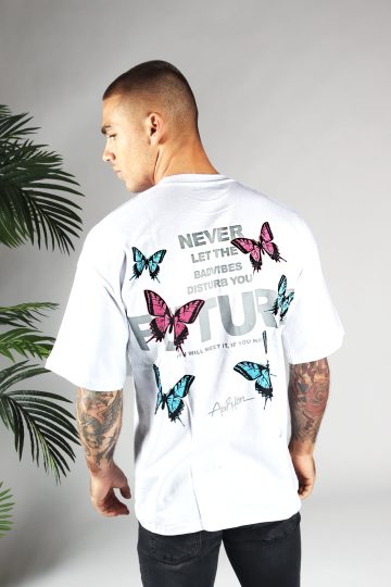 Achteraanzicht van heren T-shirt in witte kleur, met ronde hals en een oversized pasvorm. Het T-shirt is voorzien van vlinder print in roze en blauwe kleur en tekst. Het model draagt een donkere jeans.