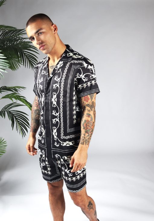 Linker zijaanzicht van model gekleed in zwarte set met witte hawai print. De set bestaat uit shorts en een blouse met korte mouwen.