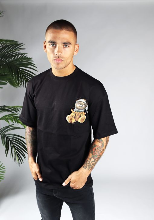 Vooraanzicht van heren T-shirt in zwarte kleur, met ronde hals en een oversized pasvorm. Het T-shirt is voorzien van een teddybeer op de linkerborst. Het model draagt een donkere jeans en heeft zijn handen in zijn broekzakken.