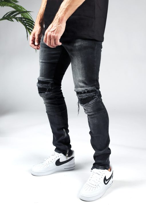 Linker zijaanzicht zwarte heren jeans slim fit model met scheuren bij de knieën en een rits aan de binnenkant van de enkel.