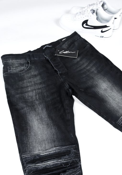 Voorkant opgevouwen zwarte heren jeans slim fit model met scheuren bij de knieën en een rits aan de binnenkant van de enkel.