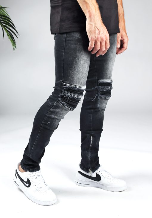 Rechter zijaanzicht zwarte heren jeans slim fit model met scheuren bij de knieën en een rits aan de binnenkant van de enkel. Gecombineerd met witte sneakers.