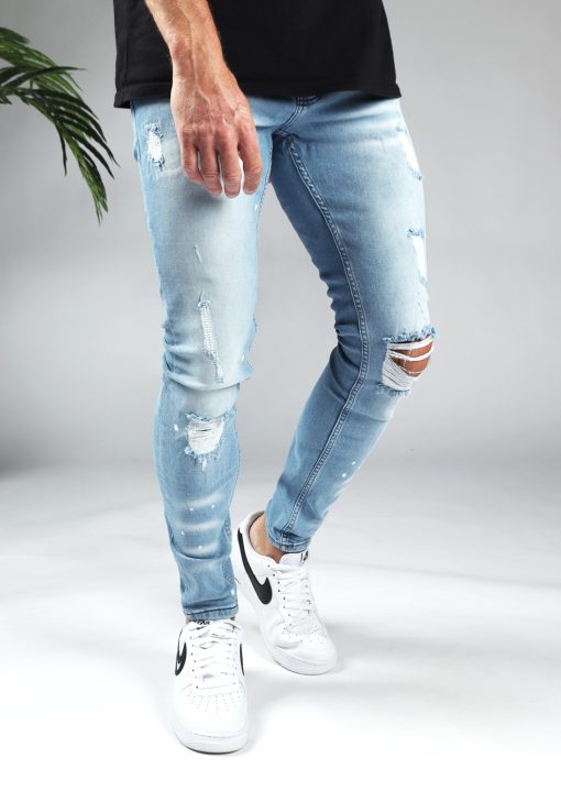 Voorzijde denim heren skinny jeans met damaged look. Gemaakt van stretch stof en voorzien van vier zakken, knoopsluiting en riemlussen. Gecombineerd met zwart T-shirt en witte sneakers.