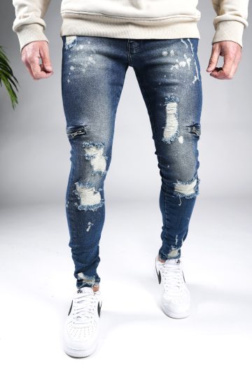 Voorkant blauwe heren skinny jeans met damaged uitstraling, scheuren in de broekspijpen en ritsen aan de zijkant van de benen. Voorzien van broekzakken, knoopsluiting en riemlussen.