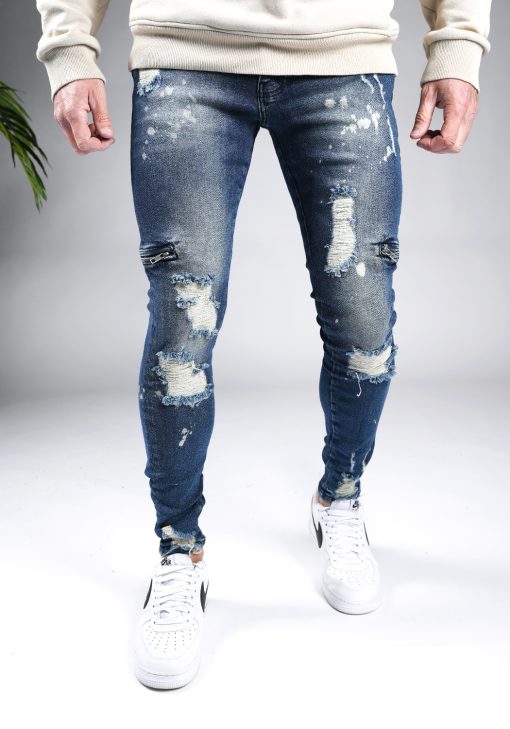 Voorkant blauwe heren skinny jeans met damaged uitstraling, scheuren in de broekspijpen en ritsen aan de zijkant van de benen. Voorzien van broekzakken, knoopsluiting en riemlussen.