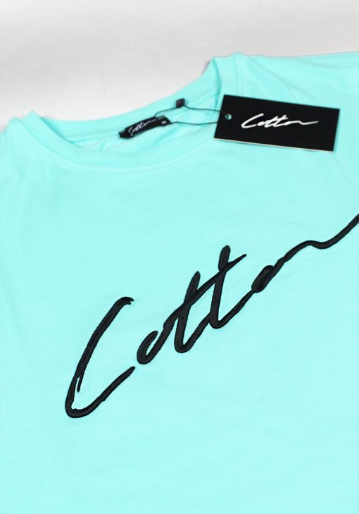 Close-up van een heren T-shirt in turquoise kleur, met ronde hals en gemaakt van katoen lycra mix stof. Het T-shirt is voorzien van het Cotton-logo op de borst in het zwart en het kledinglabel hangt aan het T-shirt.