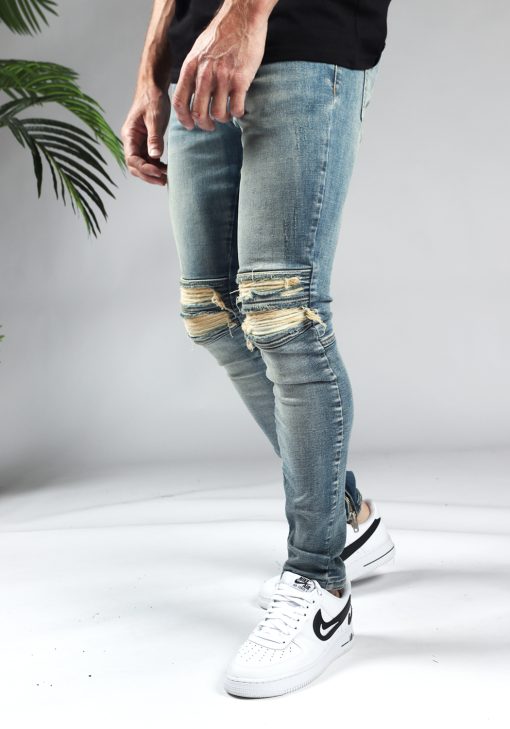 Linker zijaanzicht lichtblauwe denim heren jeans slim fit model met scheuren bij de knieën en een rits aan de binnenkant van de enkel.