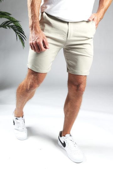 Korte broek heren chino in beige kleur met slim fit pasvorm, twee broekzakken, twee kontzakken, een knoopsluiting en riemlussen. Gecombineerd met wit T-shirt en witte gympen.