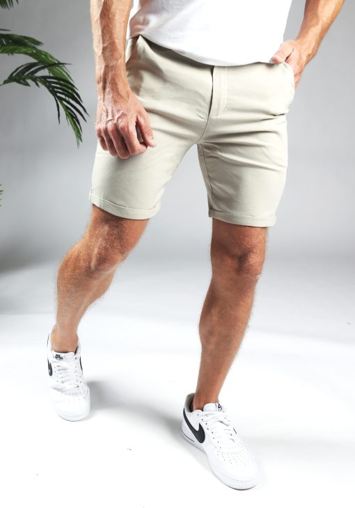 Korte broek heren chino in beige kleur met slim fit pasvorm, twee broekzakken, twee kontzakken, een knoopsluiting en riemlussen. Gecombineerd met wit T-shirt en witte gympen.