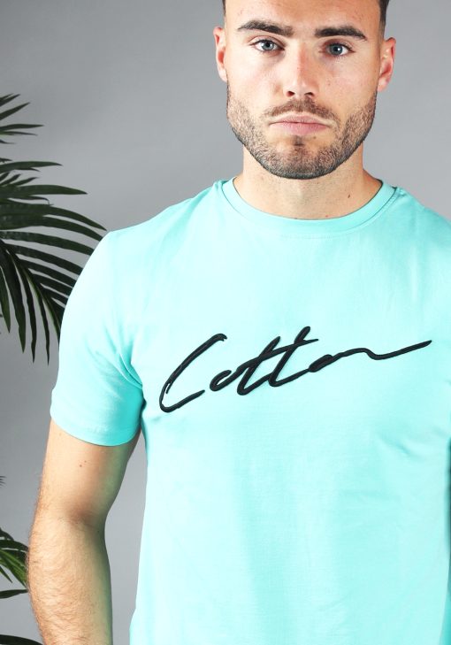 Close-up van heren T-shirt in turquoise kleur, met ronde hals en gemaakt van katoen lycra mix stof. Het T-shirt is voorzien van het Cotton-logo op de borst in het zwart.