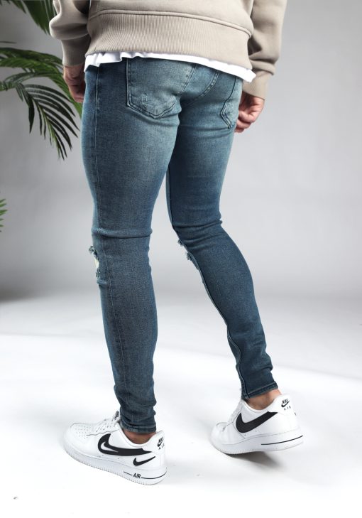 Achterkant blauwe heren skinny jeans met scheuren in de broekspijpen en gemaakt van stretch stof. Voorzien van vier zakken, knoopsluiting en riemlussen.