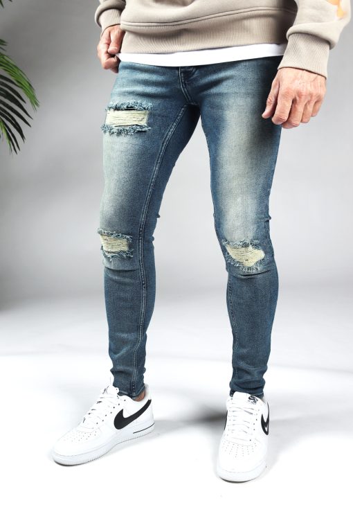 Linker zijkant blauwe heren skinny jeans met scheuren in de broekspijpen en gemaakt van stretch stof. Voorzien van vier zakken, knoopsluiting en riemlussen.