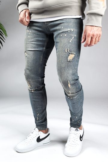 Linker zijaanzicht damaged heren skinny jeans met zandkleurige details. Voorzien van vier zakken, knoopsluiting en riemlussen.