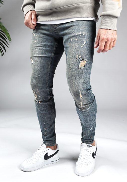 Linker zijaanzicht damaged heren skinny jeans met zandkleurige details. Voorzien van vier zakken, knoopsluiting en riemlussen.