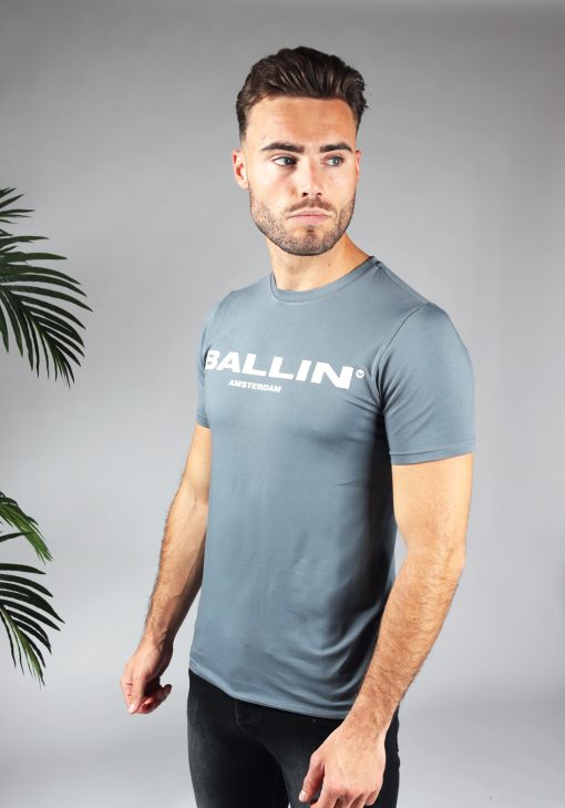Schuin vooraanzicht van model gekleed in blauw shirt met de witte tekst Ballin op de voorkant. Het model heeft zijn armen langs zich en kijkt langs zijn schouder naar links.