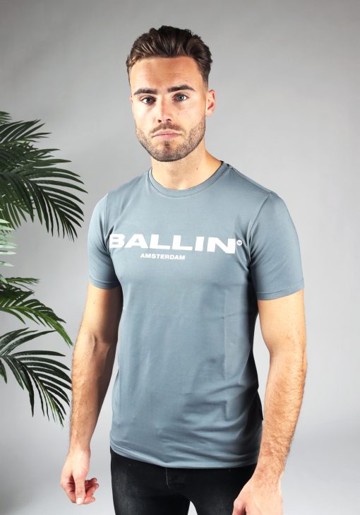 Vooraanzicht van model gekleed in blauw shirt met de witte tekst Ballin op de voorkant. Het model heeft zijn armen langs zich en kijkt in de camera.