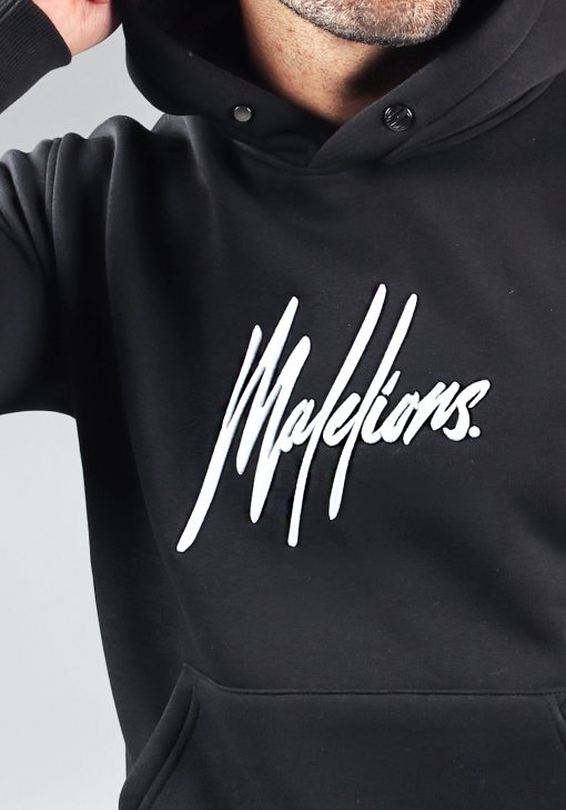 Close up vooraanzicht van model gekleed in zwarte hoodie met het grote witte Malelions logo op de borst.