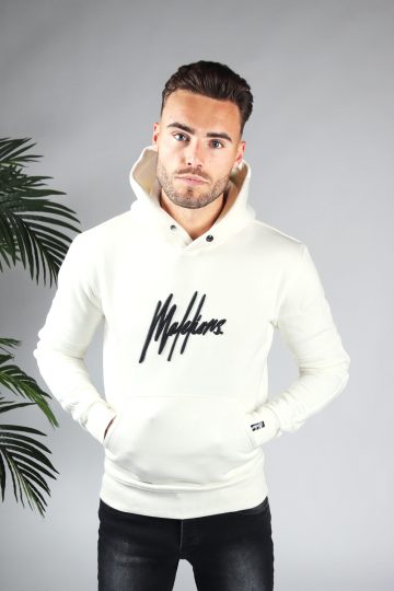 Vooraanzicht van model gekleed in witte hoodie met het grote zwarte Malelions logo op de borst. Het model heeft zijn handen in de hoodie pocket en kijkt recht in de camera.