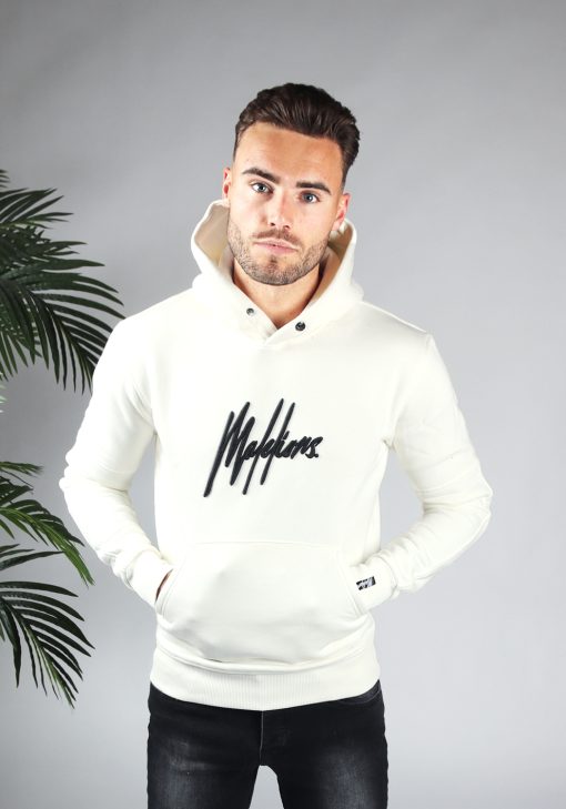 Vooraanzicht van model gekleed in witte hoodie met het grote zwarte Malelions logo op de borst. Het model heeft zijn handen in de hoodie pocket en kijkt recht in de camera.