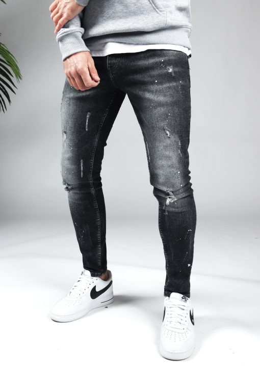 Voorkant zwarte denim damaged heren skinny jeans, gemaakt van stretch stof. Voorzien van vier zakken, knoopsluiting en riemlussen. Gecombineerd met grijze hoodie en witte sneakers.
