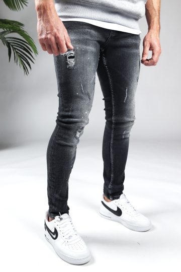Rechter zijaanzicht zwarte denim damaged heren skinny jeans, gemaakt van stretch stof. Voorzien van vier zakken, knoopsluiting en riemlussen. Gecombineerd met grijze sweater en witte sneakers.