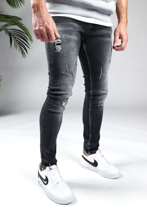 Rechter zijaanzicht zwarte denim damaged heren skinny jeans, gemaakt van stretch stof. Voorzien van vier zakken, knoopsluiting en riemlussen. Gecombineerd met grijze sweater en witte sneakers.