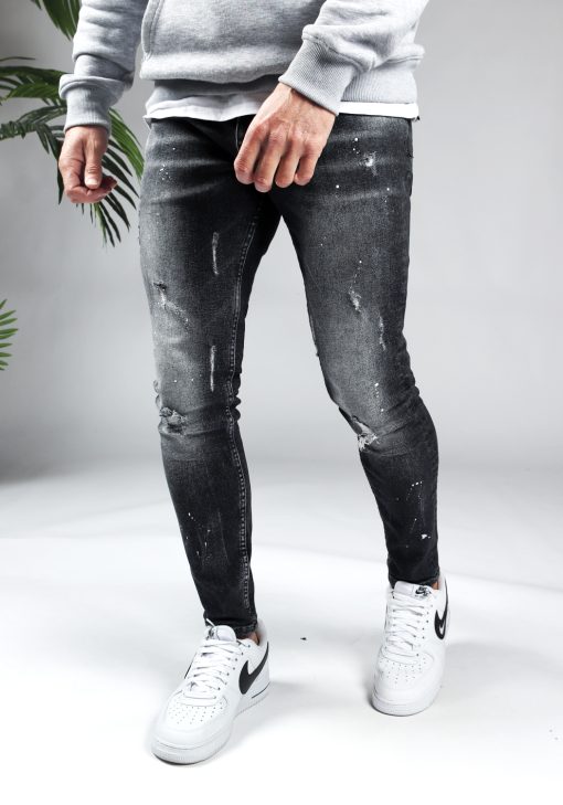 Voorkant zwarte denim damaged heren skinny jeans, gemaakt van stretch stof. Voorzien van vier zakken, knoopsluiting en riemlussen. Gecombineerd met grijze hoodie en witte sneakers.