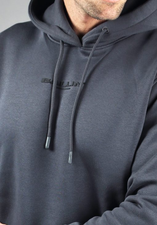 Close up vooraanzicht van model gekleed in een blauw-grijze hoodie met de zwarte tekst "Ballin" in het midden van de borst.