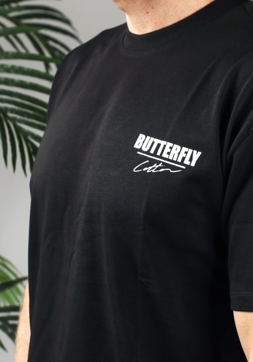 Close-up van een heren T-shirt in zwarte kleur, met een ronde hals en gemaakt van stevige katoenen stof. Het T-shirt is voorzien van tekst en het Cotton-logo op de linkerborst.