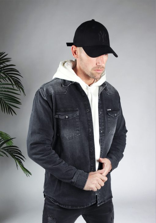 Schuin vooraanzicht van model gekleed in een witte hoodie met daar overheen een grijze spijker jack. Het model heeft zijn handen voor zich en hij kijkt naar naar de grond.