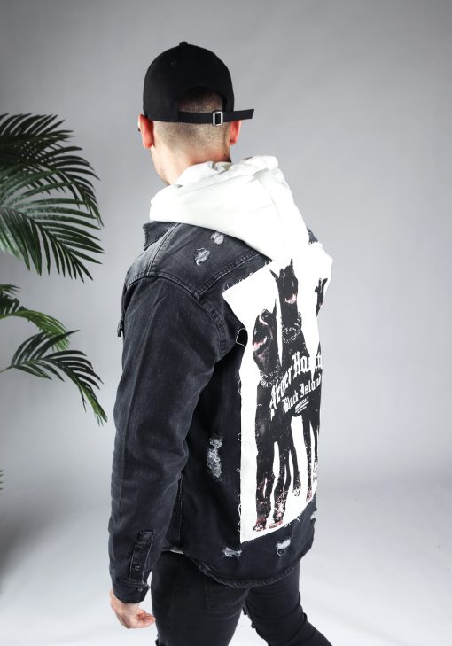 Schuin achteraanzicht van model gekleed in een witte hoodie met daar overheen een grijze spijker jack met op de rug een dobberman hondenprint met tekst. Het model heeft zijn armen langs zich.