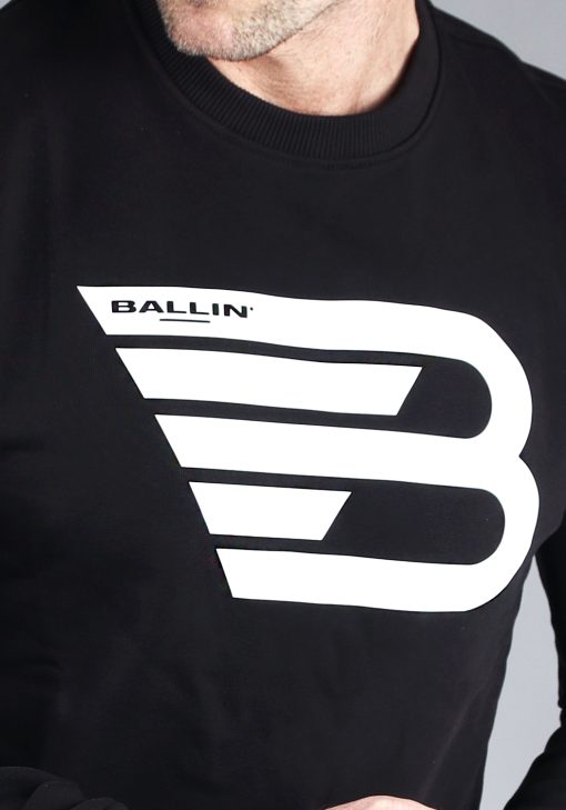 Close up van model gekleed in zwarte sweater met het grote witte Ballin logo in het midden van de borst.