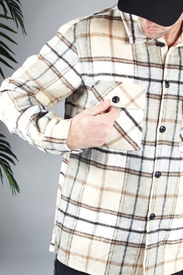 Closeup van borstzak met zwarte knoop van beige flannel met ruitenpatroon. Het model draagt een zwarte pet, kijkt naar de borstkas, en houdt zijn hand op het borstzakje.