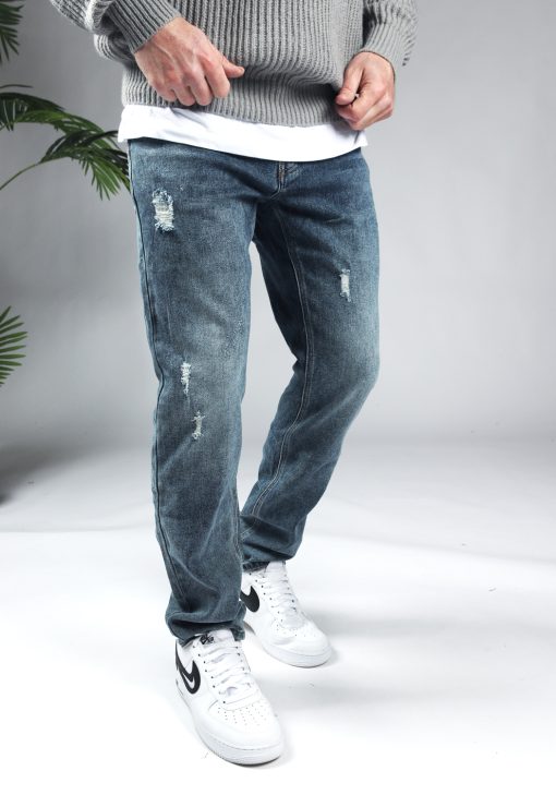Rechter zijaanzicht blauwe denim heren jeans met loose fit en damaged uitstraling, gecombineerd met grijze hoodie en witte sneakers