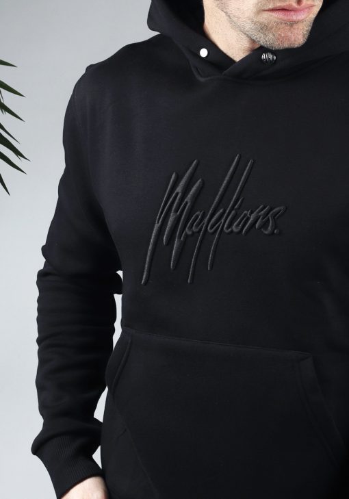 Close up van zwarte hoodie met een zwart geborduurd logo van Malelions op de borst.